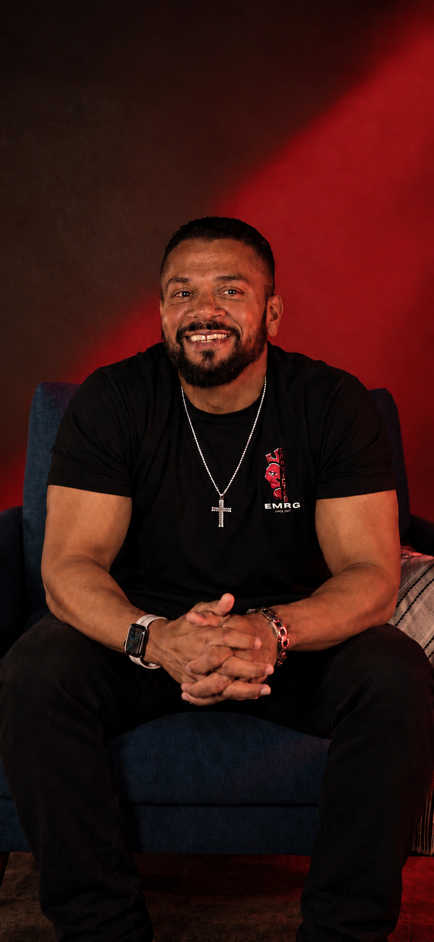 Jason Godinho seated for a portrait in a dark room with warm red light.